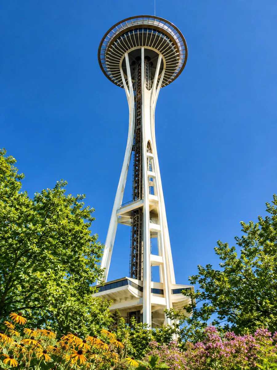 Die Space Needle vor tiefblauem Himmel, von unten gesehen, mit Bäumen und Blumen
