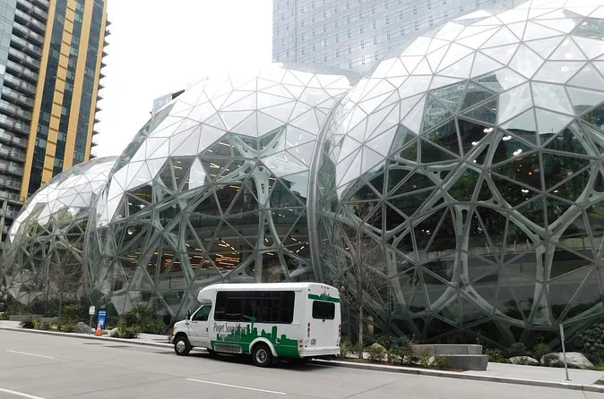 A small white tour shuttle parked beside the glass Amazon Spheres